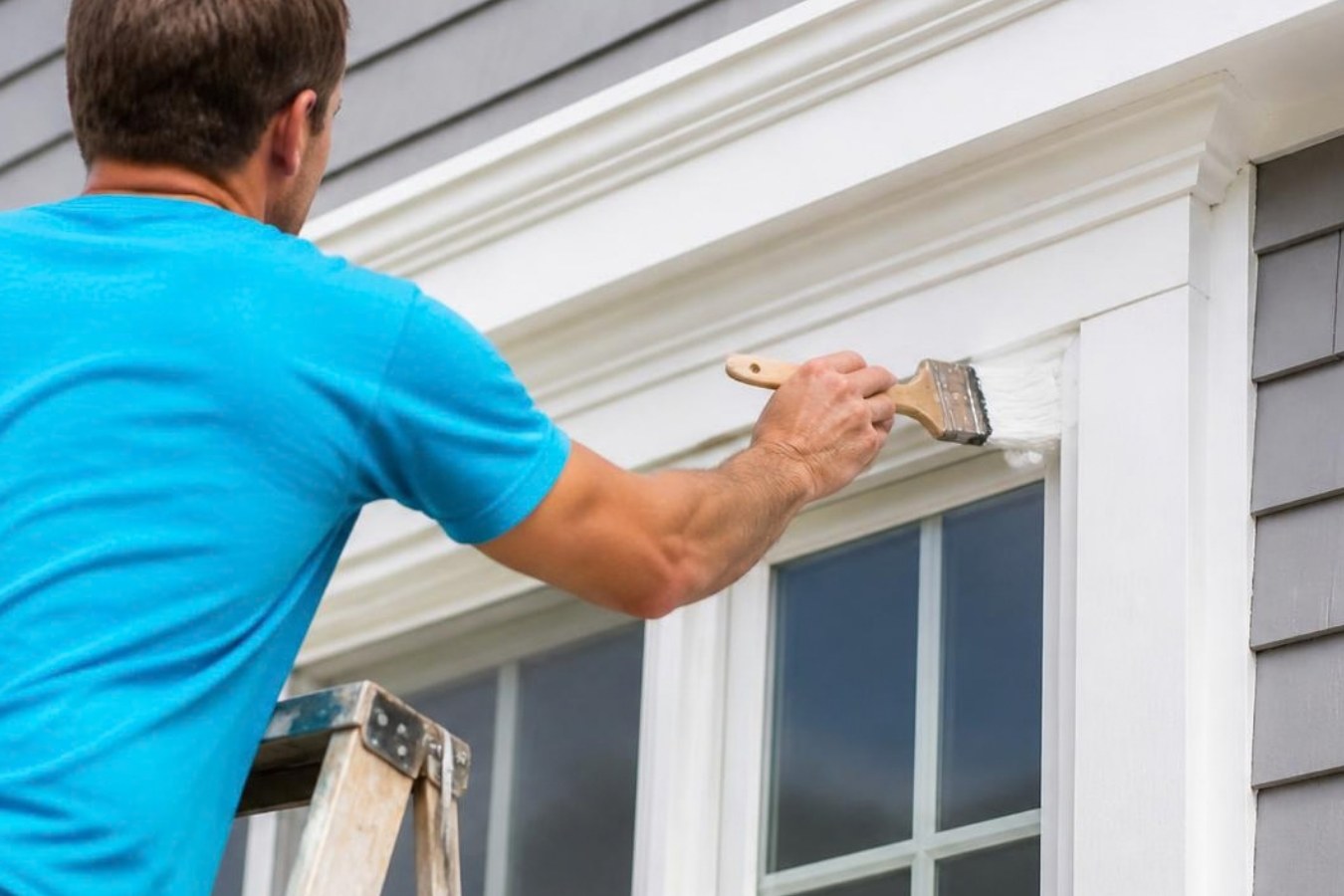 Painter brushing fresh white paint onto window trim